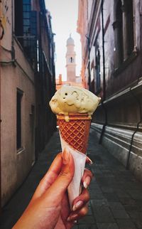 Hand holding ice cream cone against buildings in city