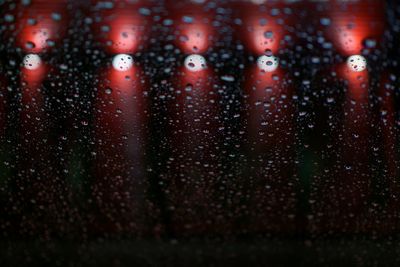 Illuminated lights seen through wet glass window during rainy season at night