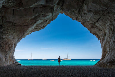 Rear view of woman standing in cave at beach against sea and sky