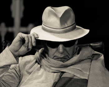 Close-up of man wearing hat against black background