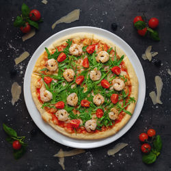 Traditional italian pizza with homemade tomato sauce, roasted shrimp, cherry tomato and arugula
