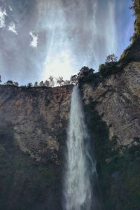 Low angle view of waterfall against cloudy sky