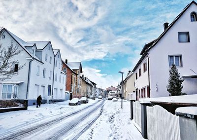 Snow covered road by buildings against sky