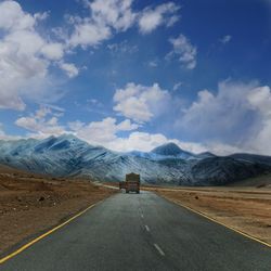 Trucks on road leading towards mountains against sky