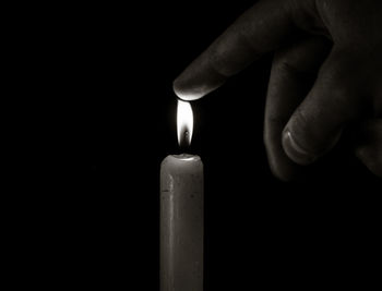 Cropped hand of person touching flame of candle in darkroom