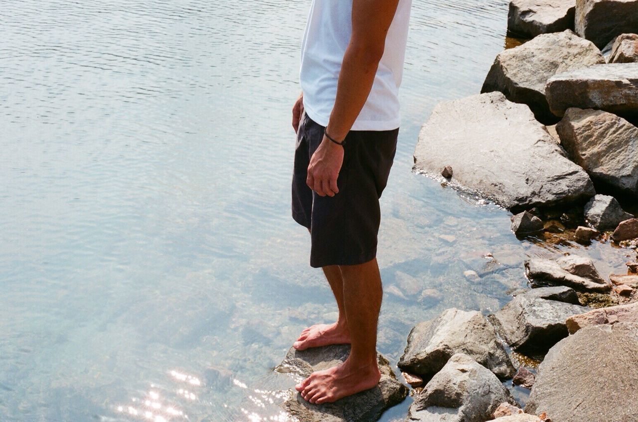 water, lifestyles, leisure activity, full length, standing, low section, casual clothing, person, high angle view, walking, day, outdoors, wet, sunlight, reflection, rear view, beach