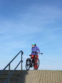 Woman standing by bicycle against blue sky