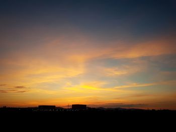 Silhouette of city against cloudy sky during sunset