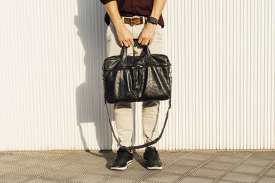 Businessman holding shoulder bag while standing on footpath