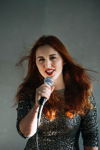 Portrait of redhead female singer woman in sparkly evening dress holding microphone on dark night