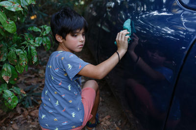 Close view of girl with short black haircut washing blue car in the garden