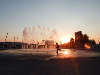 People on shore against clear sky during sunset