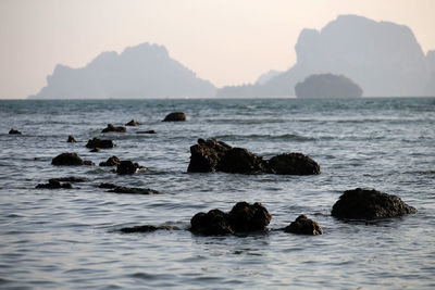 Rocks in sea against sky during sunset