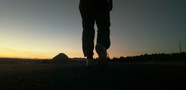 Low section of silhouette man standing on field against sky