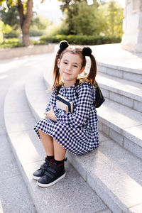 Cute young child girl 5-6 year old wear checkered black and white dress and backpack holding books 