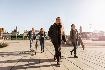 Teenagers walking on footpath against clear sky in city