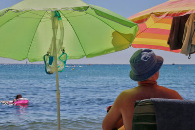 Rear view of man sitting on chair at beach