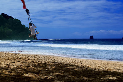 Man swinging at beach against sky