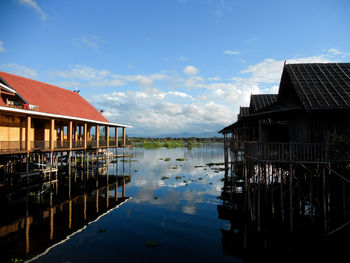 Wooden house by lake against sky