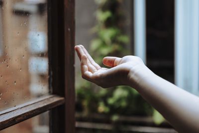 Cropped hand of person at window during rainy season