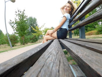 Portrait of smiling young woman sitting on wood against sky