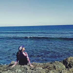 Woman sitting in sea against clear sky