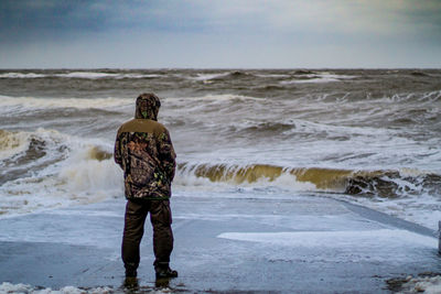 Rear view of man standing at beach against sky