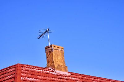 Low angle view of antenna on roof against clear blue sky