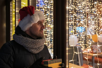Man wearing santa hat holding gift box by window