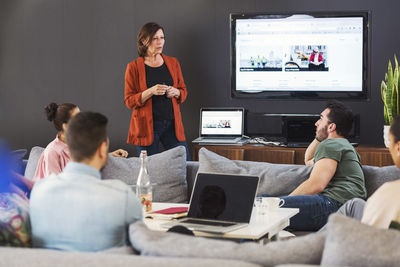 Mature businesswoman in front of television giving presentation to colleagues in office lobby