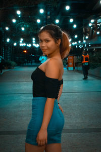 Portrait of smiling young woman standing in city at night