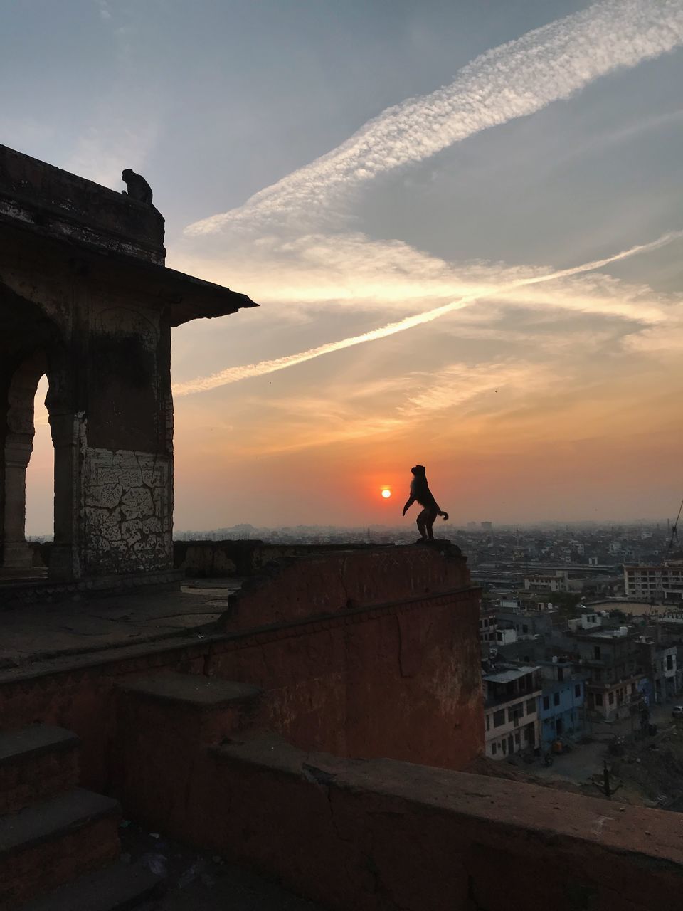 MAN STANDING BY BUILDING AGAINST SKY DURING SUNSET