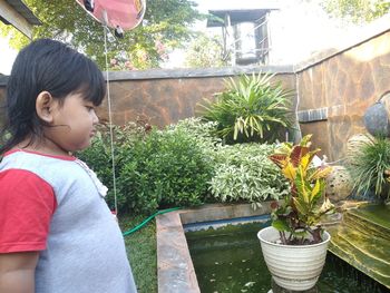 Side view of girl looking at potted plants in yard