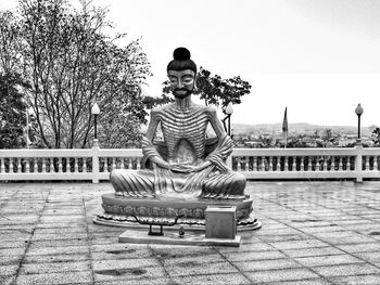 Statue of man sitting against built structure