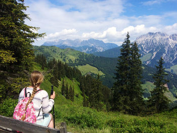 Rear view of woman looking at mountains and trees against sky