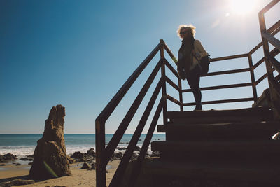 Woman standing on stairs at beach against sky