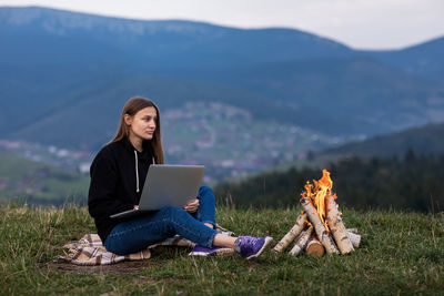 Young woman using laptop while sitting on field