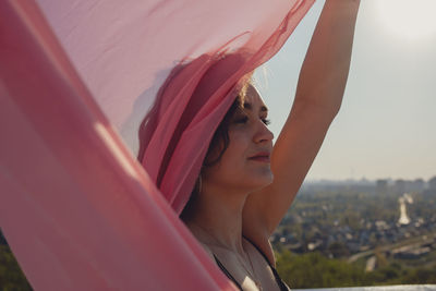 Young woman with pink scarf standing against sky during sunset