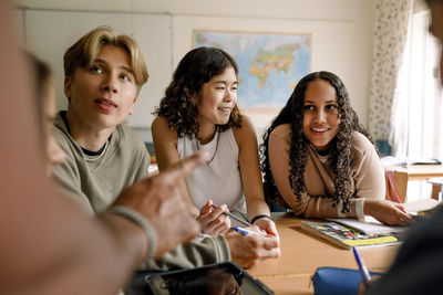 Smiling teenage girl looking at male teacher talking in classroom