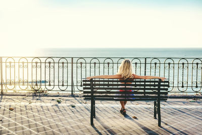 Rear view of woman sitting on beach against clear sky