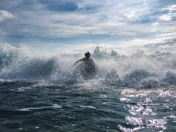 Scenic view of man surfing and splashing in sea against sky