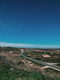 High angle view of road amidst field against blue sky