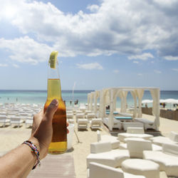 Midsection of woman holding drink at beach against sky