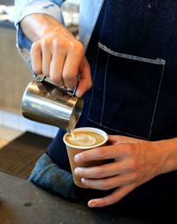Midsection of barista pouring coffee in cafe