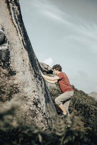 Side view of man on rock against sky