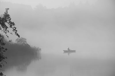 Silhouette person riding boat on lake in foggy weather