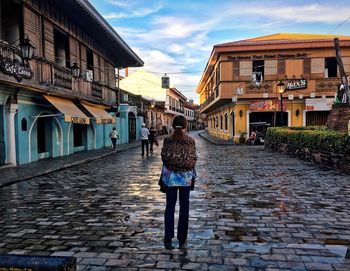 Full length rear view of woman walking on cobblestone