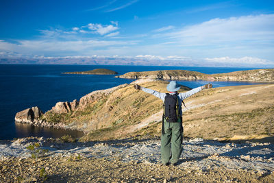Rear view of man with arms outstretched standing by sea against sky
