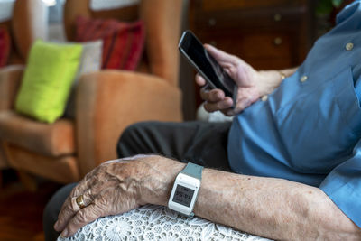 Elderly man using a mobile phone and wearing a smart emergency alarm bracelet around wrist at home