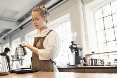 Female barista pouring boiling water in coffee filter at cafe